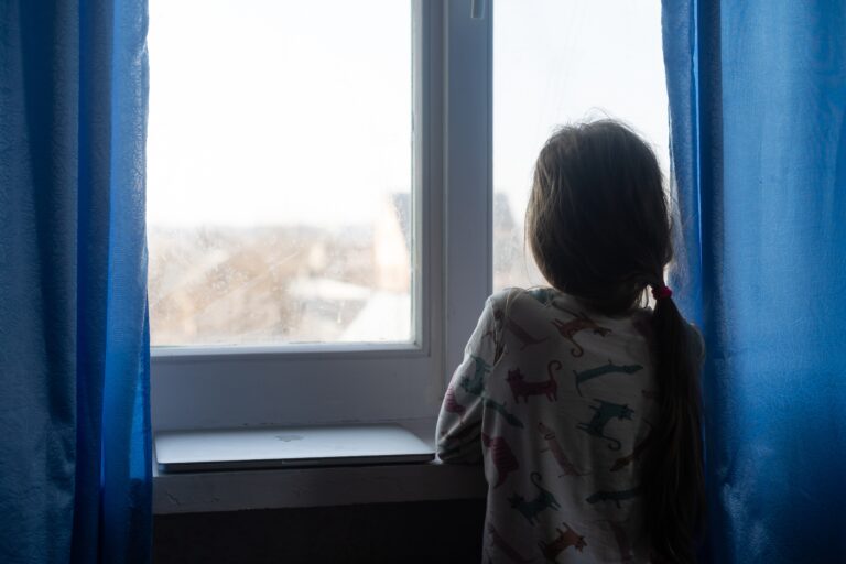 child looking out a window depressed